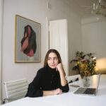 Young woman in elegant office setting with laptop and flowers on desk, exuding a professional vibe.